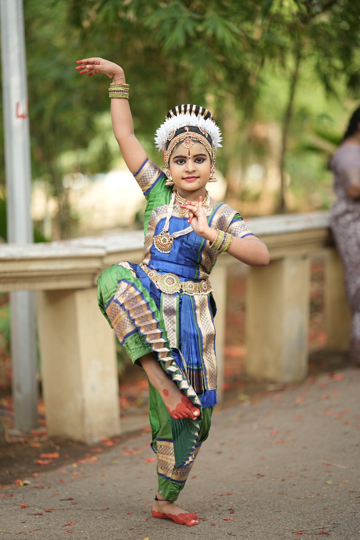 Young student in green and blue costume holding a balance pose